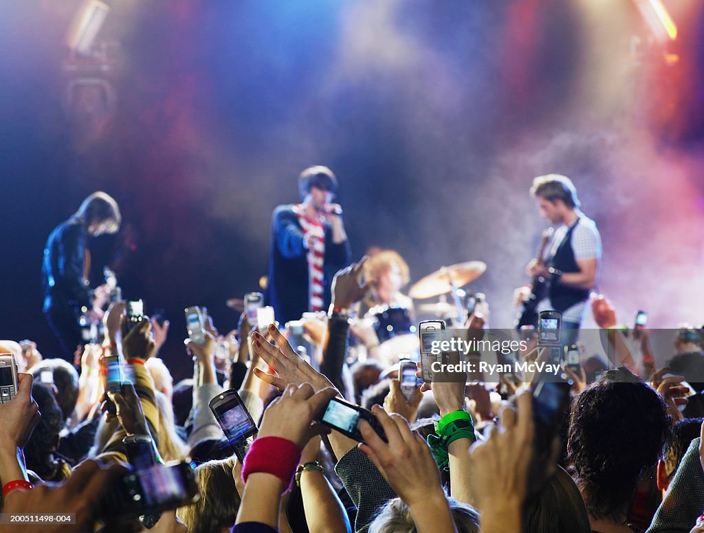 Band performing on stage, audience holding up hands in foreground