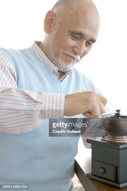 senior man preparing coffee using mill grinder, smiling, - sleeveless sweater stock pictures, royalty-free photos & images