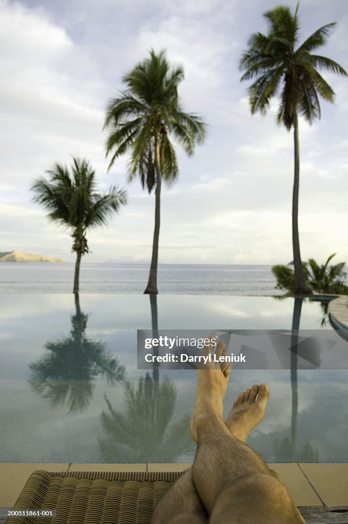 Fiji, man sitting on lounge chair beside infinity pool, low section