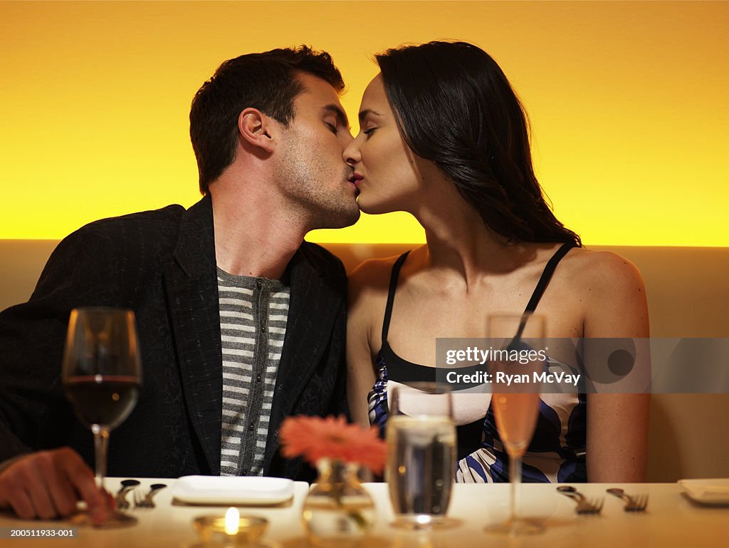 Young man and woman kissing at table in nightclub, eyes closed