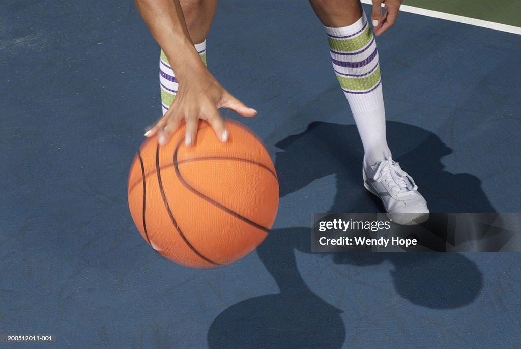 Woman standing dribbling basketball, low section, blurred motion