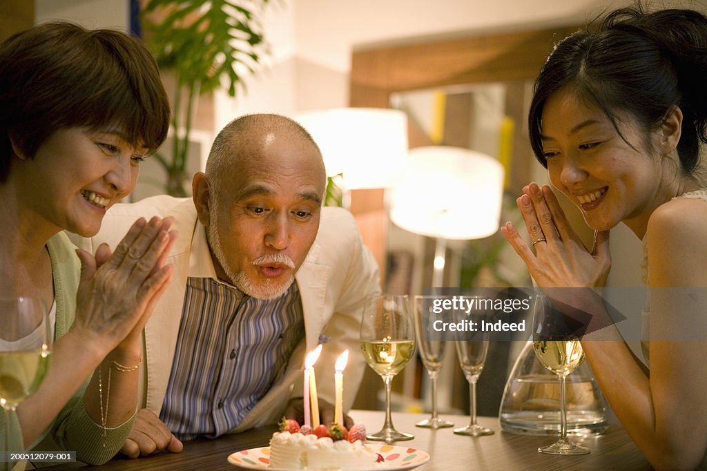 Senior man blowing out candles on birthday cake at dinner table