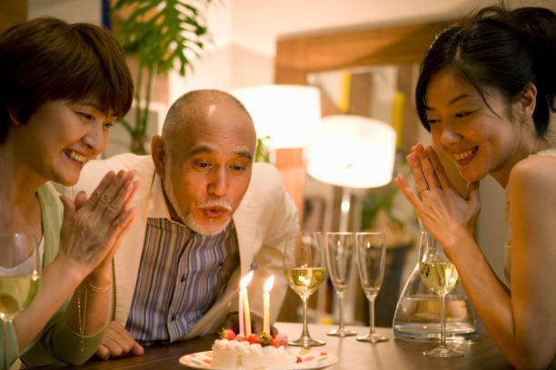 senior man blowing out candles on birthday cake at dinner table - sweet white wine stock pictures, royalty-free photos & images