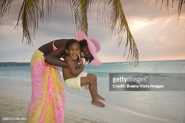 mother playing with daughter (3-5) on swing, sunset - jamaican girl stock pictures, royalty-free photos & images