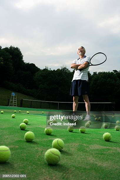 senior man standing on tennis court, holding racquet, arms folded - large group of objects sport stock pictures, royalty-free photos & images