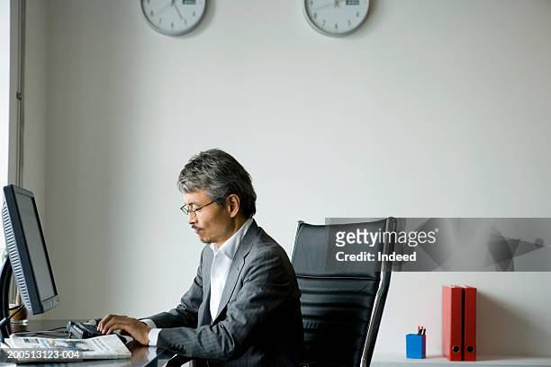mature businessman typing on keyboard, side view - clock person desk stockfoto's en -beelden