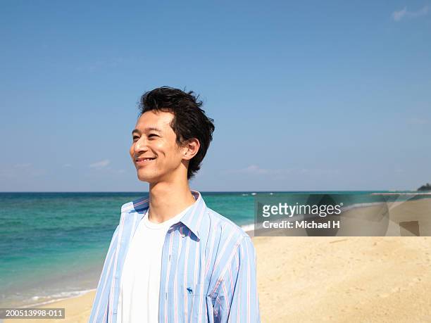 young man standing on beach, smiling, looking away - 24 h du mans stock-fotos und bilder