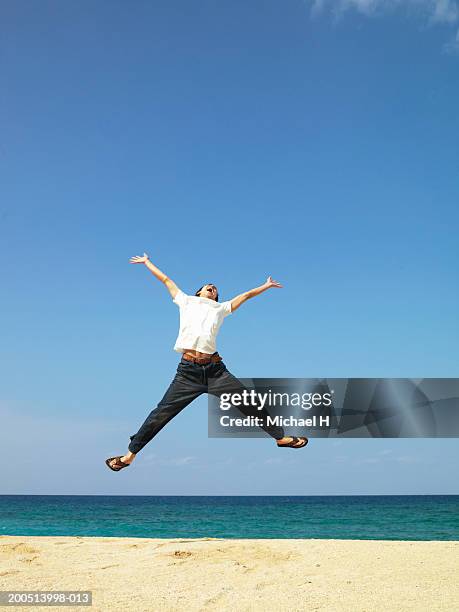 young man jumping in midair on beach, arms raised - 24 h du mans bildbanksfoton och bilder