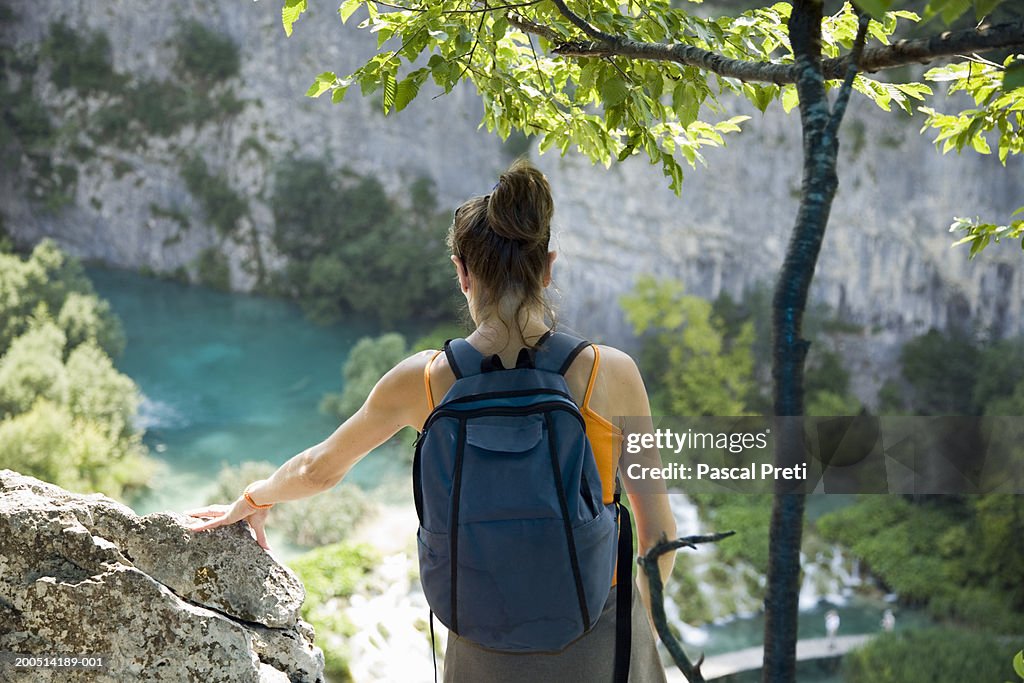 Woman standing with rucksack, looking down at lake, rear view