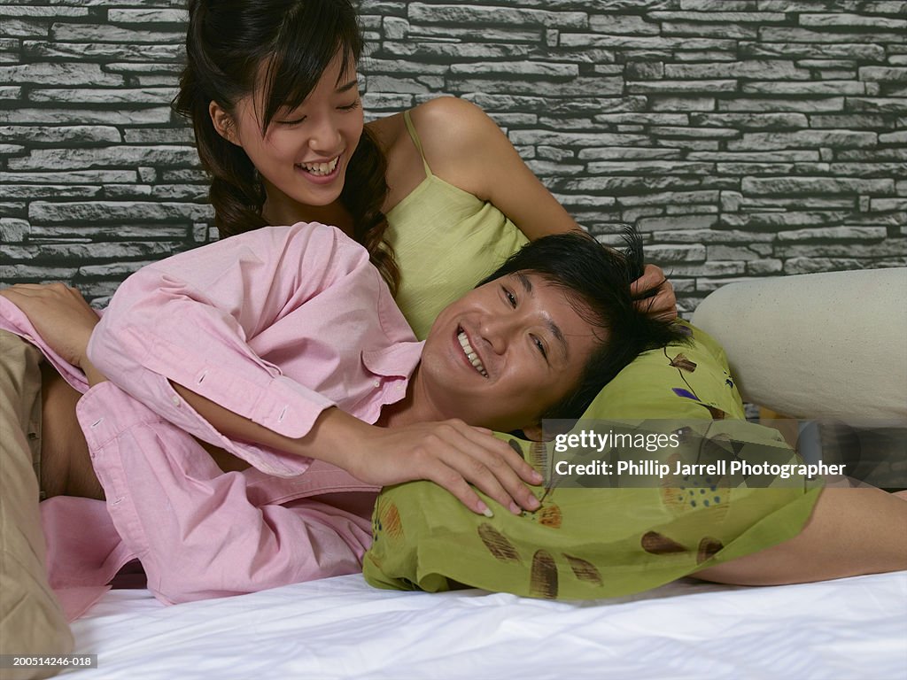 Young couple on bed, man lying on woman's lap, smiling