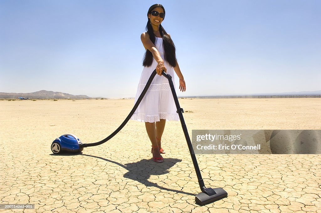 Young woman vacuuming desert, smiling