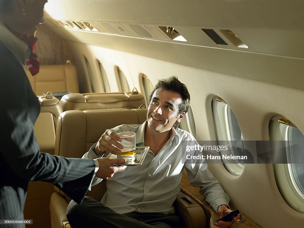 Flight attendant giving drink to businessman on private plane