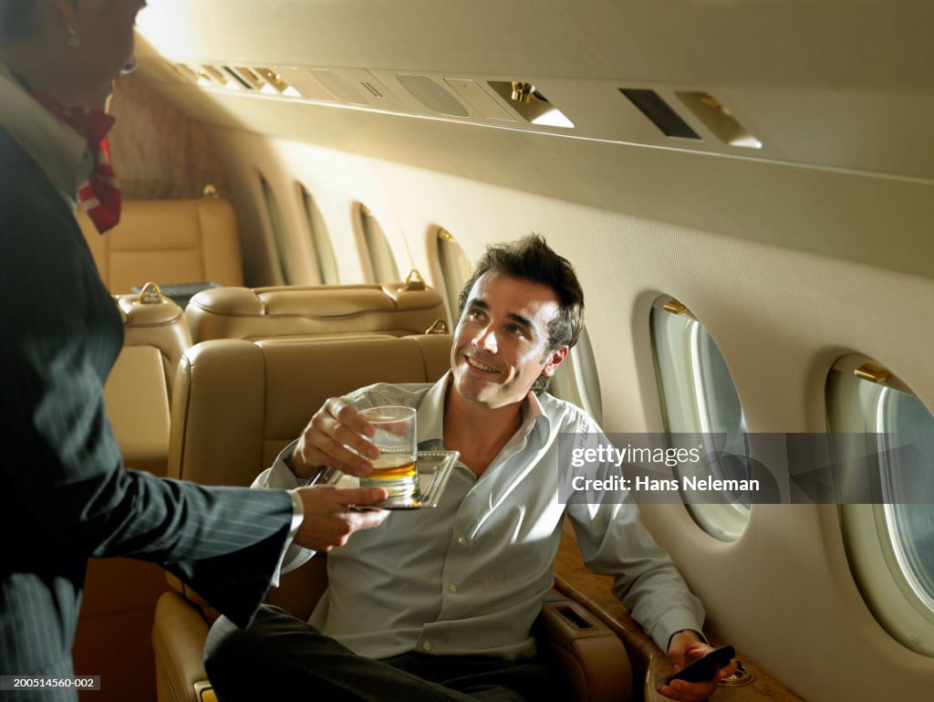 Flight attendant giving drink to businessman on private plane