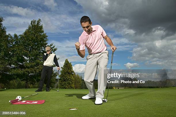 two men playing golf, one standing by hole in foreground celebrating - playing to win ストックフォトと画像