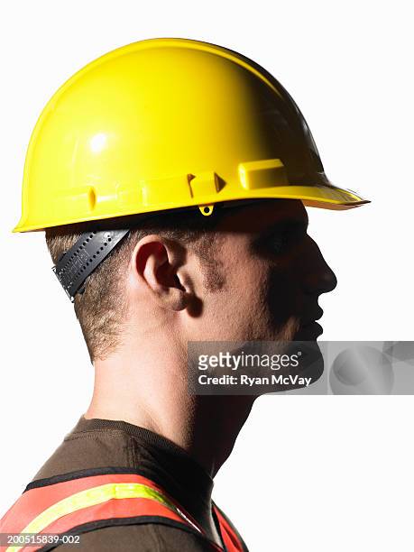 young male construction worker wearing hardhat, side view - helm stock-fotos und bilder