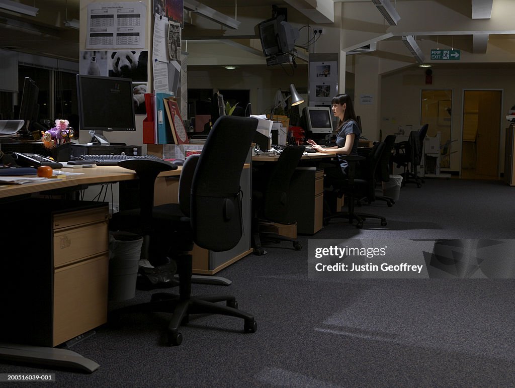 Young woman working in dark office, with lamp, side view
