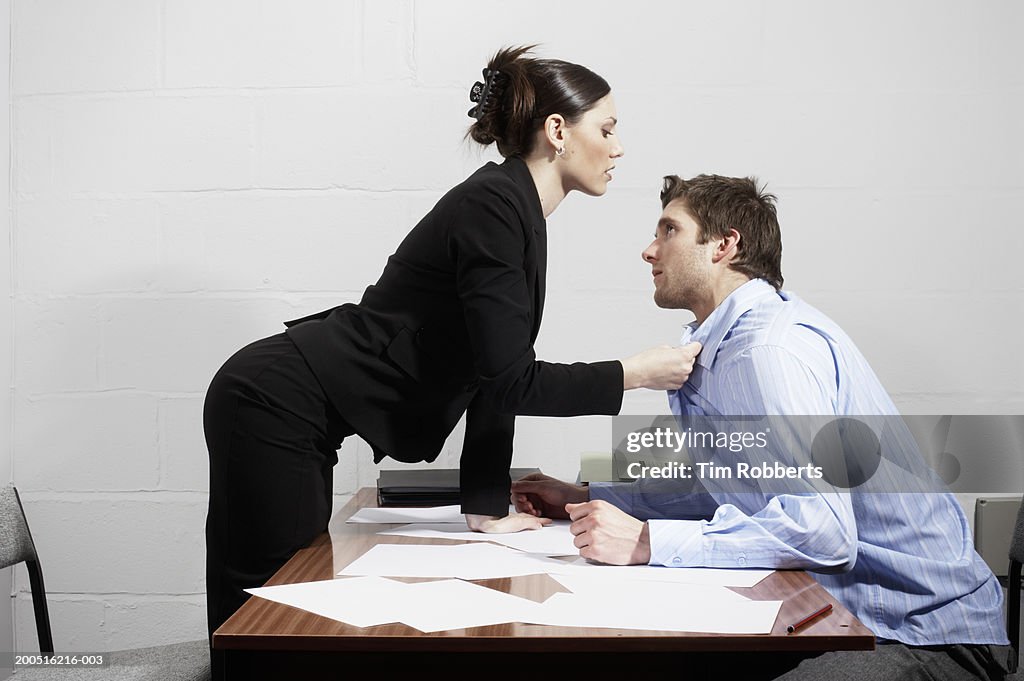 Business woman grabbing collar of business man over desk, side view