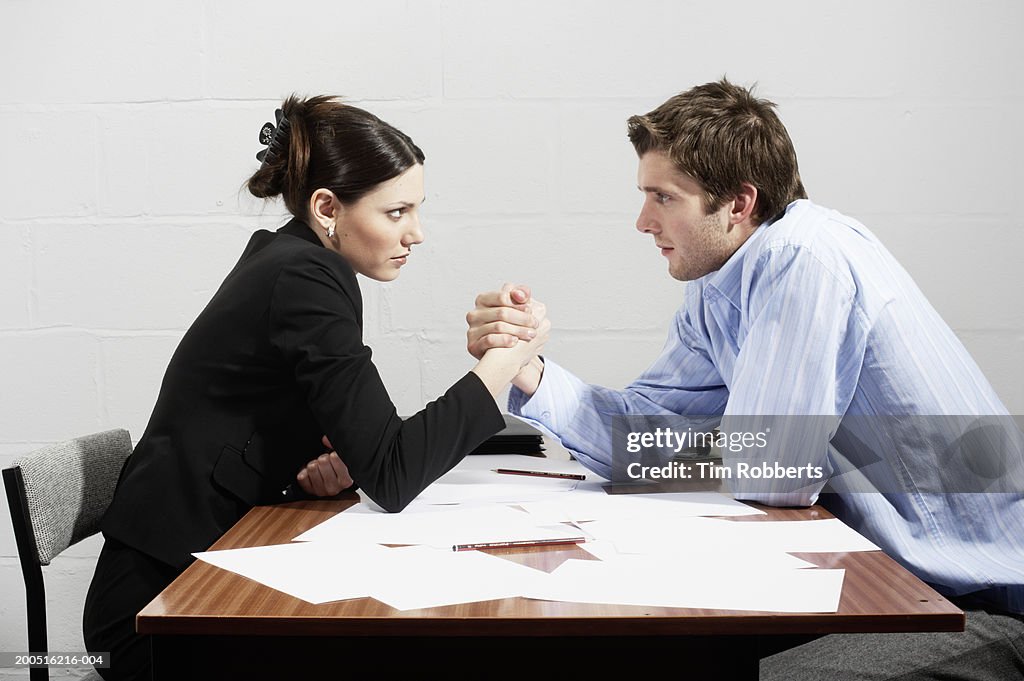 Business woman and business man arm wrestling over table, side view