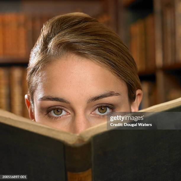 young woman looking over book in library, portrait - hardbound stock pictures, royalty-free photos & images