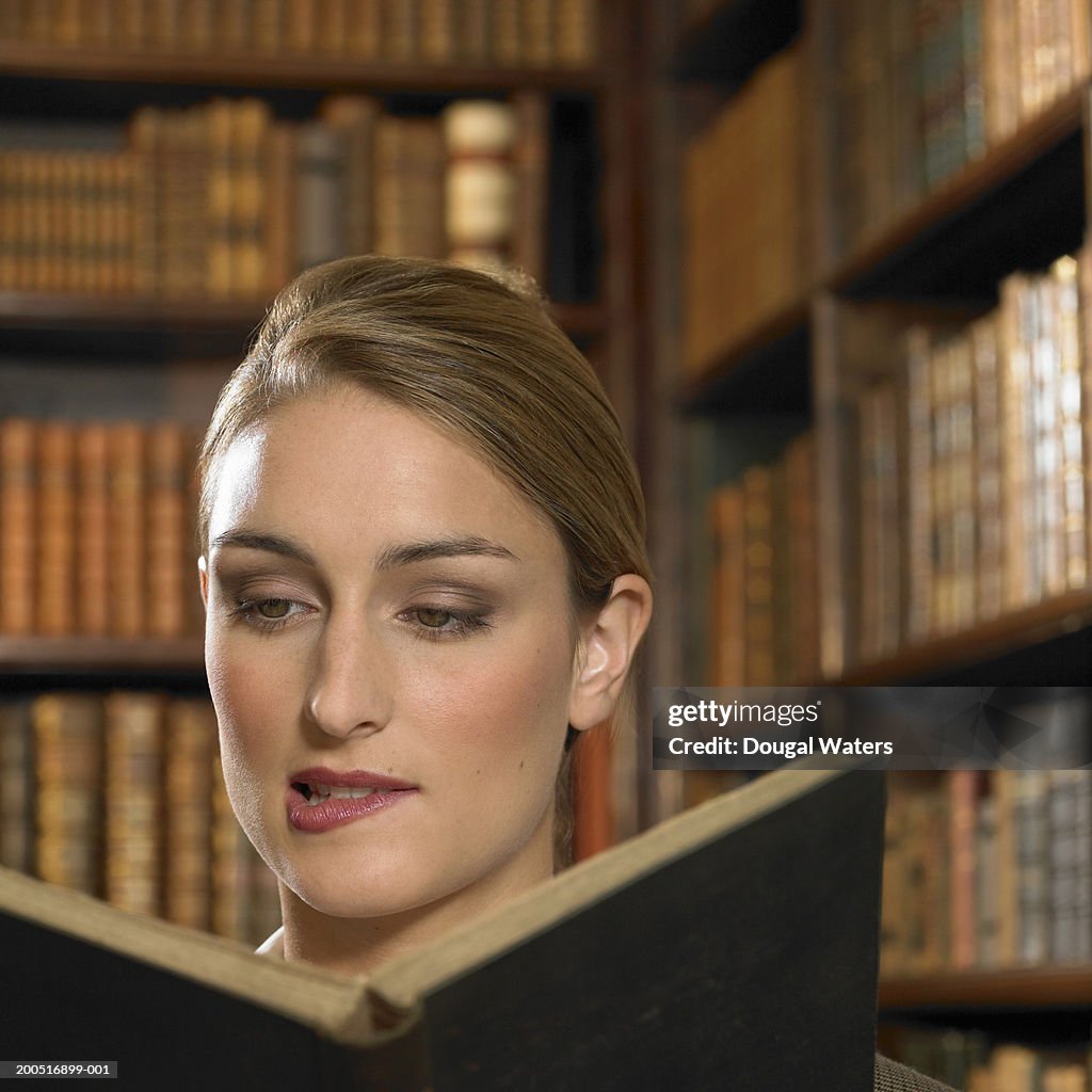 Young woman biting lip as she reads book in library
