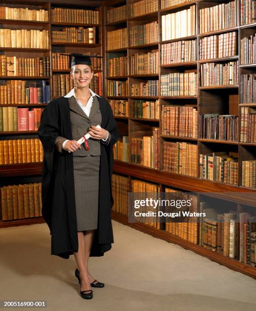 young woman in cap and gown in library, smiling, portrait - hardbound stock pictures, royalty-free photos & images