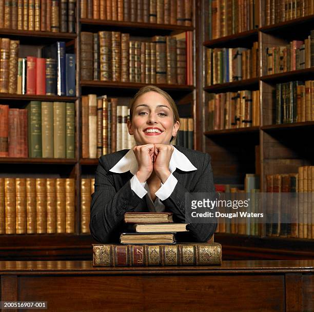 young woman leaning on books in library, smiling, portrait - hardbound stock pictures, royalty-free photos & images