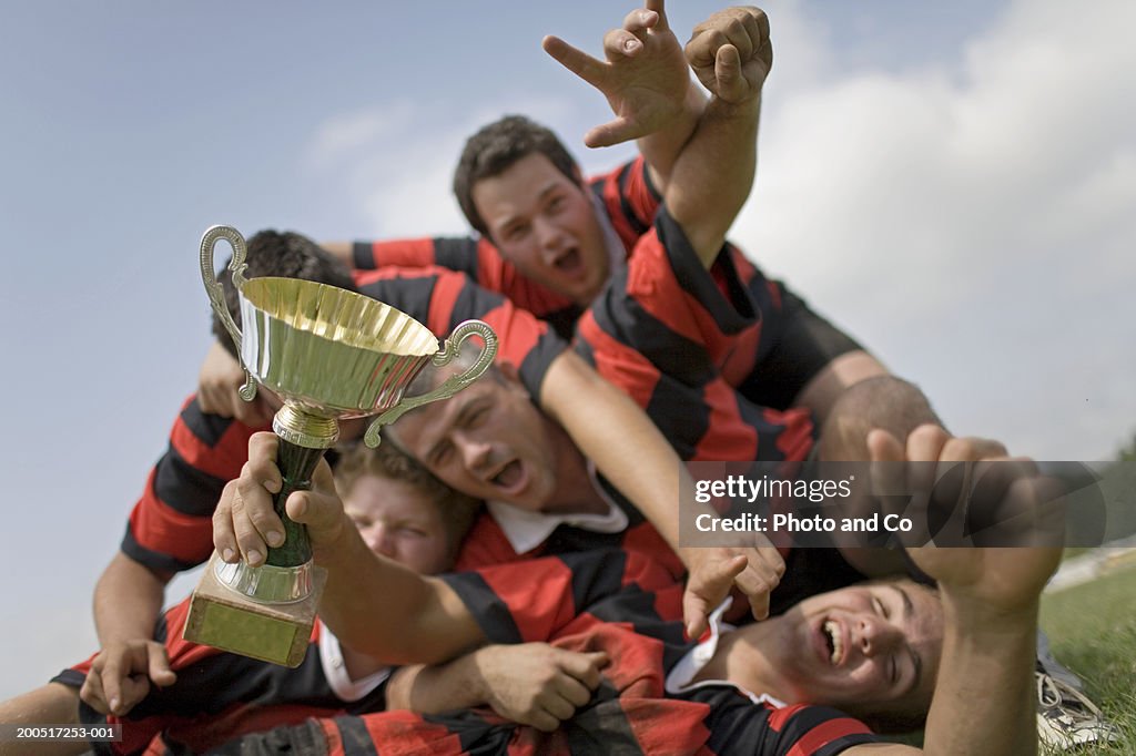 Rugby team celebrating on pitch with trophy, cheering, low angle view