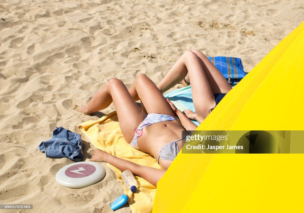 Two young women lying on beach, obscured by yellow sunshade