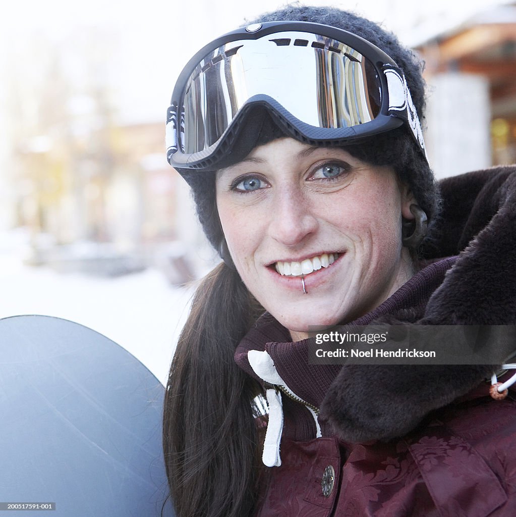 Young woman with snowboard wearing ski goggles, smiling, portrait