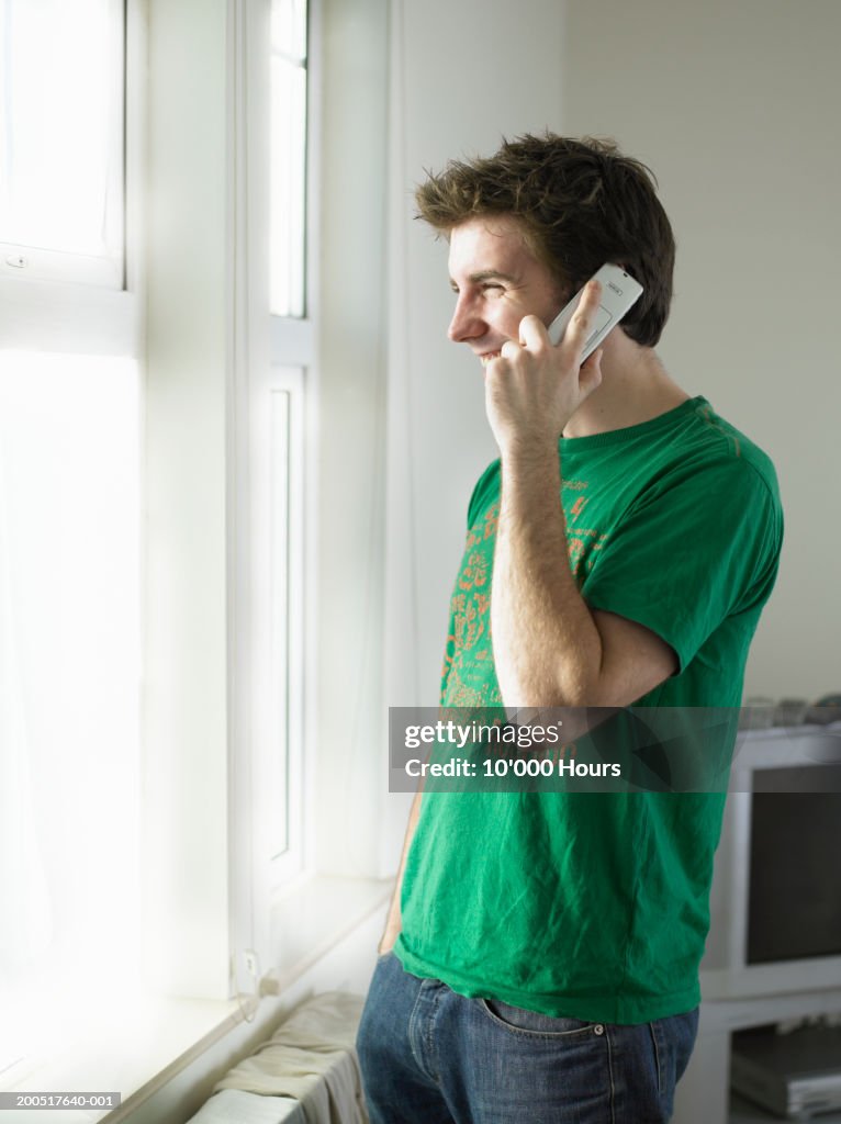 Young man using mobile phone by window