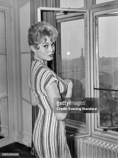 French actress Brigitte Bardot standing at the window of her room at the Savoy Hotel, London, October 27th 1956. She is in London to attend the 1956...