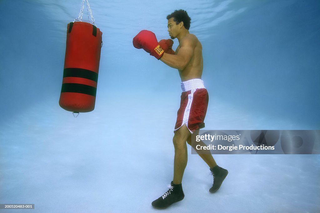 Man boxing in pool, with punch bag, underwater view
