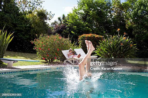 senior man diving into pool, senior woman sitting on sun lounger - old couple jumping stock-fotos und bilder