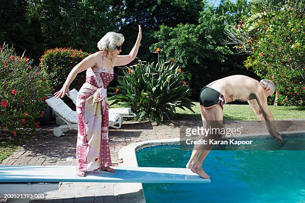 senior woman pushing senior man off diving board, side view - trampolino piscina foto e immagini stock