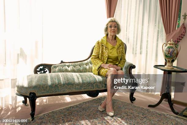 senior woman sitting on sofa, portrait - legs crossed at ankle stock-fotos und bilder