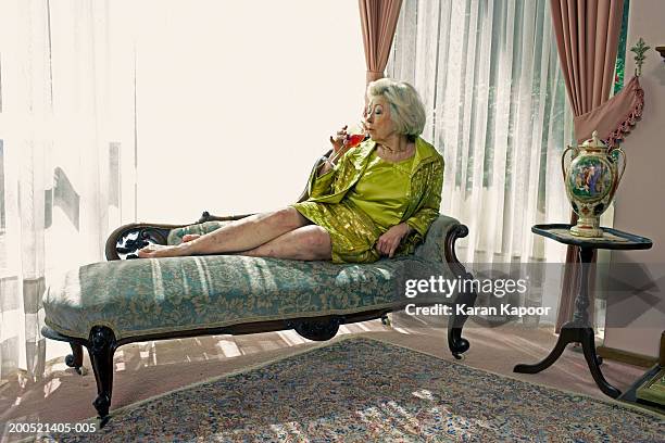 senior woman sitting on sofa, drinking wine, side view - chaise longue stock pictures, royalty-free photos & images