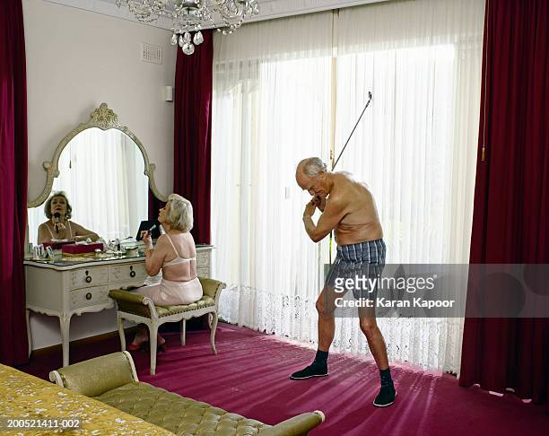 senior woman applying makeup and senior man swinging golf club - golf stock-fotos und bilder