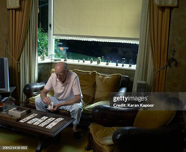senior man sitting on sofa, playing cards, elevated view - solitaire fotografías e imágenes de stock