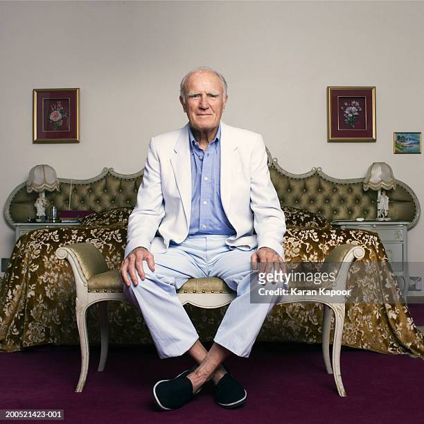 senior man sitting on chair in bedroom, portrait - sitzen stock-fotos und bilder