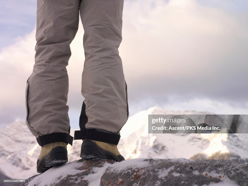 Mature man standing on snow-covered rock, low section, rear view