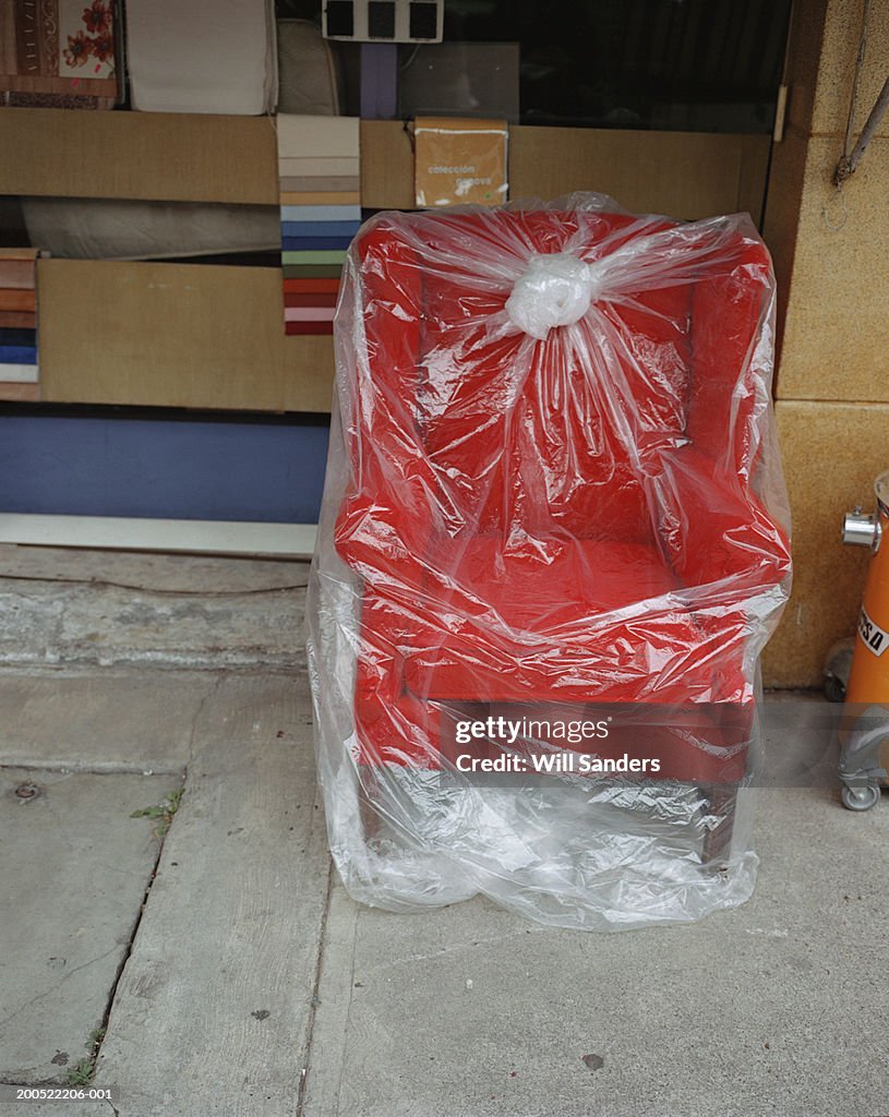 Red armchair wrapped in plastic on pavement