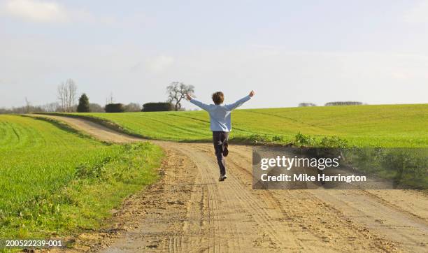 boy (8-10) running on country road, arms outstretched, rear view - child boy arms out stock pictures, royalty-free photos & images