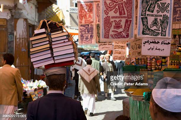 yemen, bookseller walking with books balanced on head in market - yemen stock pictures, royalty-free photos & images