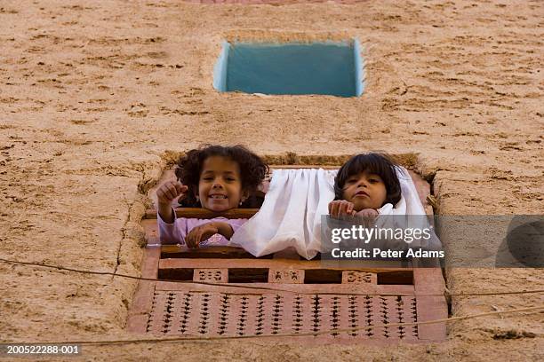 yemen, boy and girl (6-8) leaning out of window, smiling, portrait - jemen stockfoto's en -beelden