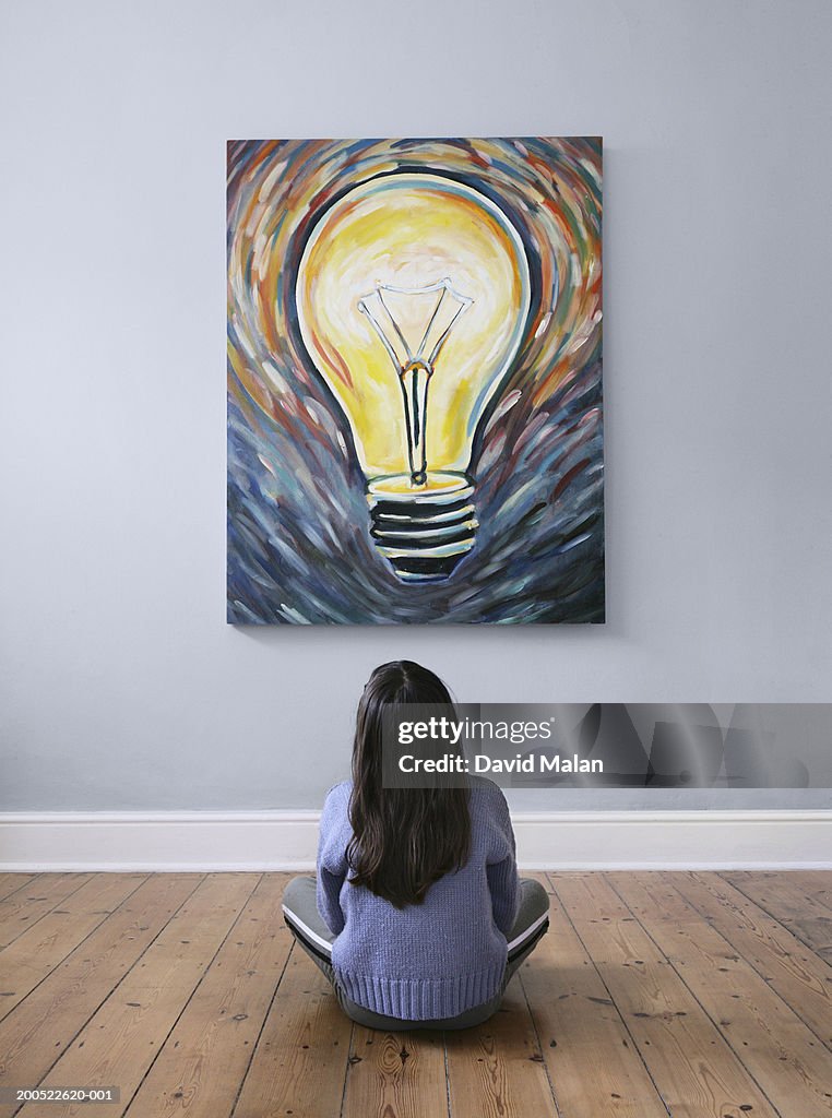 Girl (7-9) sitting on floor in front of painting of lightbulb