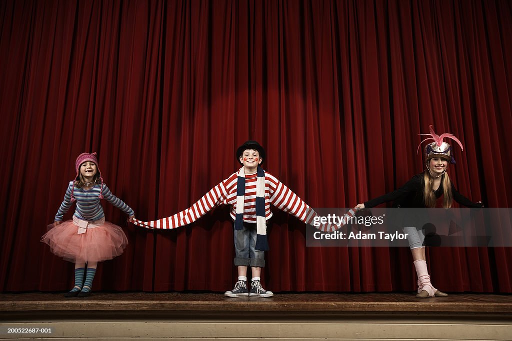 Two girls and boy (6-10) in costume taking bow on stage, smiling