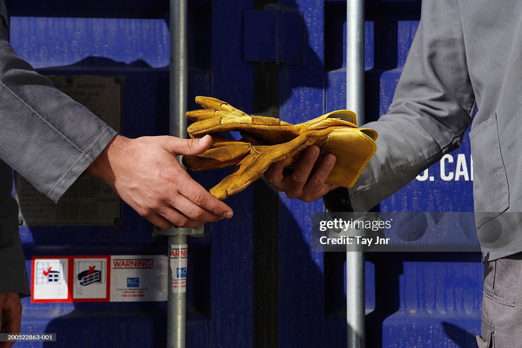 Two men passing gloves beside cargo container, mid section