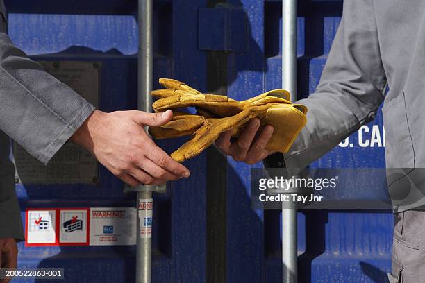 two men passing gloves beside cargo container, mid section - glove stock pictures, royalty-free photos & images