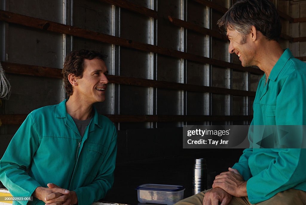 Two men resting on lorry, smiling, side view