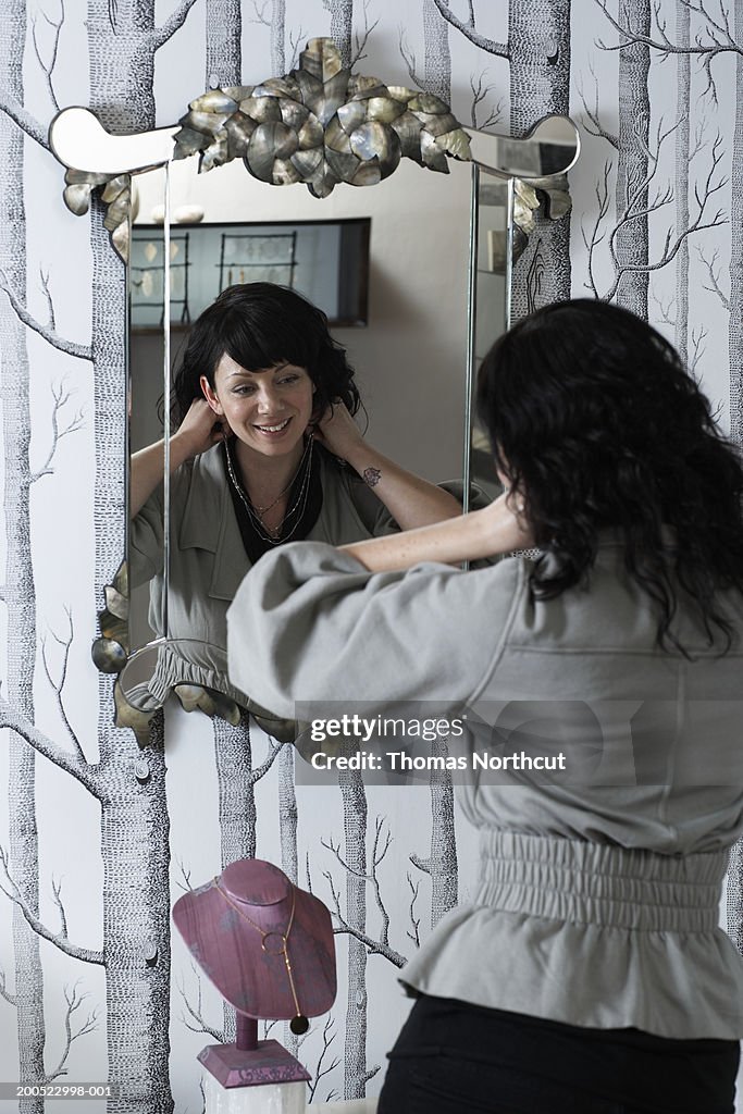 Woman trying on necklace in front of mirror in retail store, rear view